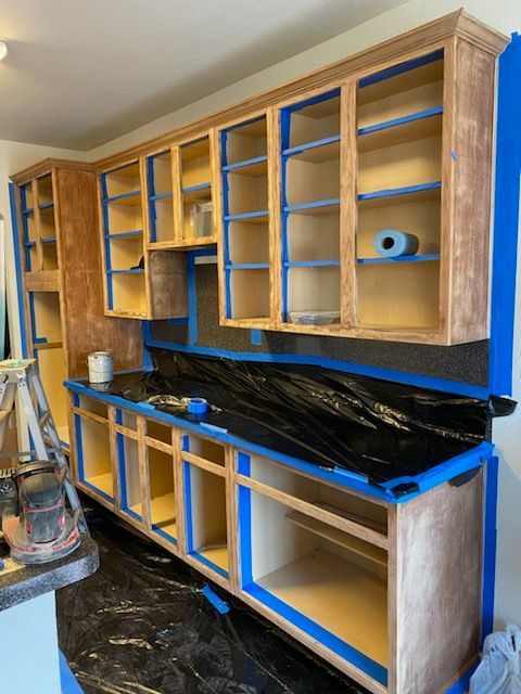 Kitchen mid-renovation with cabinets stripped bare and counters covered